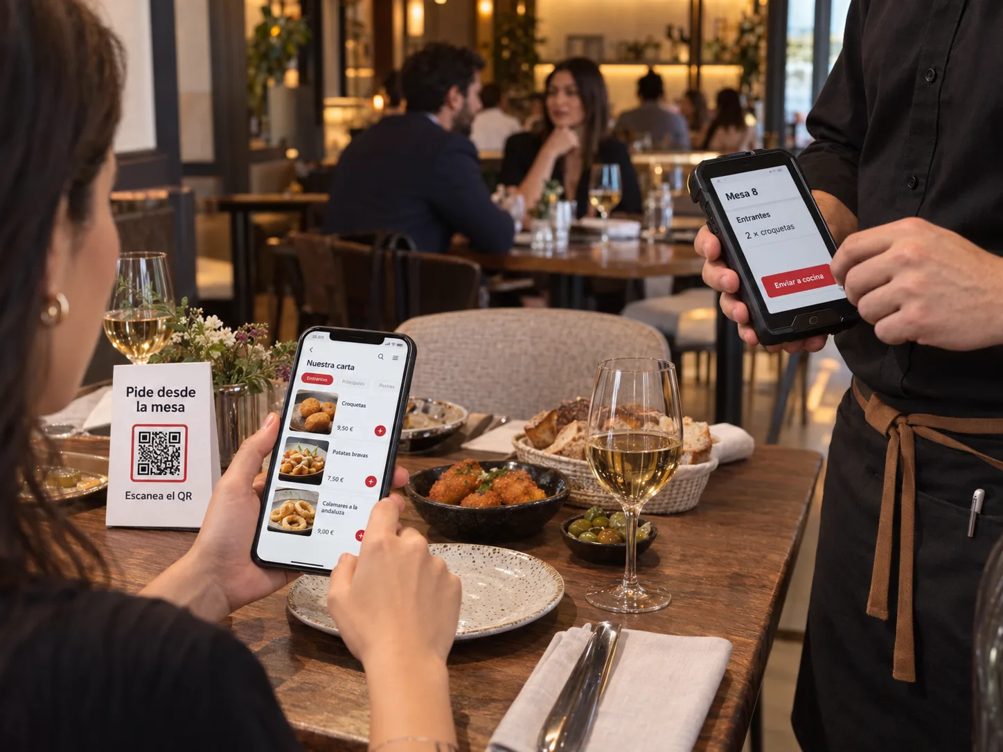 Sala de un restaurante: un cliente pide desde el QR de su mesa mientras un camarero toma otro pedido con la PDA