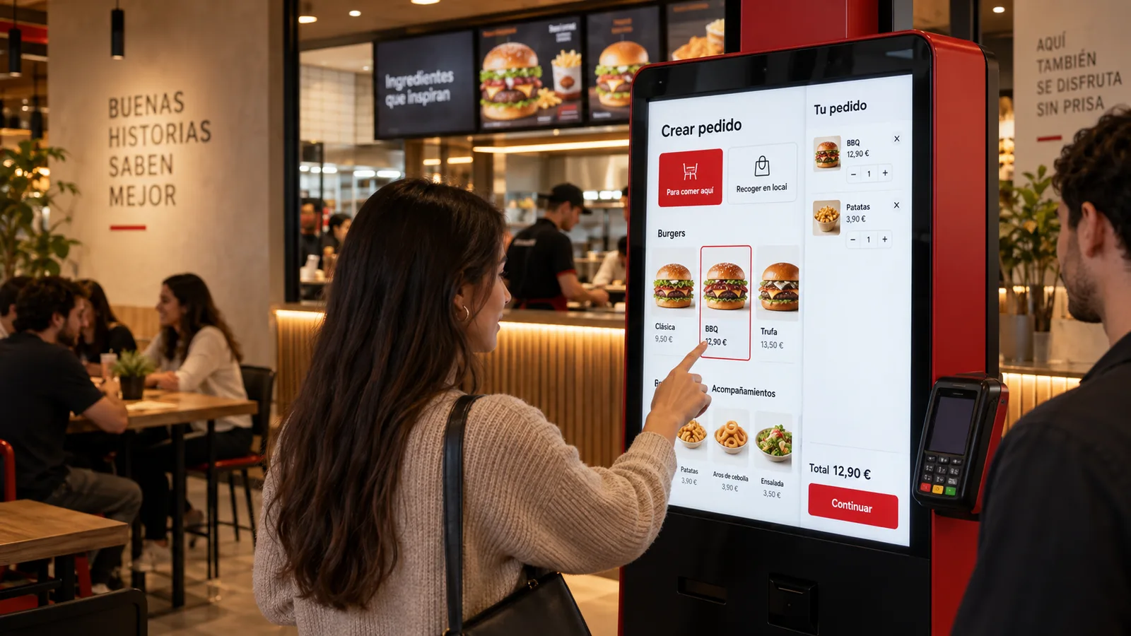 Una clienta pide en el kiosco de autopedido de un restaurante, con la carta en pantalla y el datáfono al lado